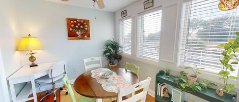 A dining area with a wooden table, white chairs, a ceiling fan, and a window with blinds.