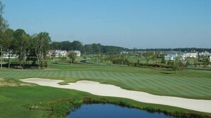 A golf course with sand bunkers, a pond, and houses in the background.