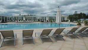 A pool area with lounge chairs and umbrellas, a covered seating area, and a building in the background.