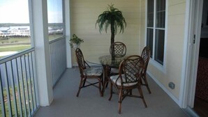 A balcony with a glass table and wicker chairs, a potted plant, and a view of a building in the background.