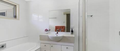 A modern bathroom with a white bathtub, a large sink with a mirror above it, and a glass-enclosed shower area.