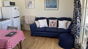 A compact living space with a kitchenette, a blue sofa, a dining table with a checkered tablecloth, and a window with floral curtains. - Amazing Views Pet Friendly Bed and Breakfast (Good Hope)