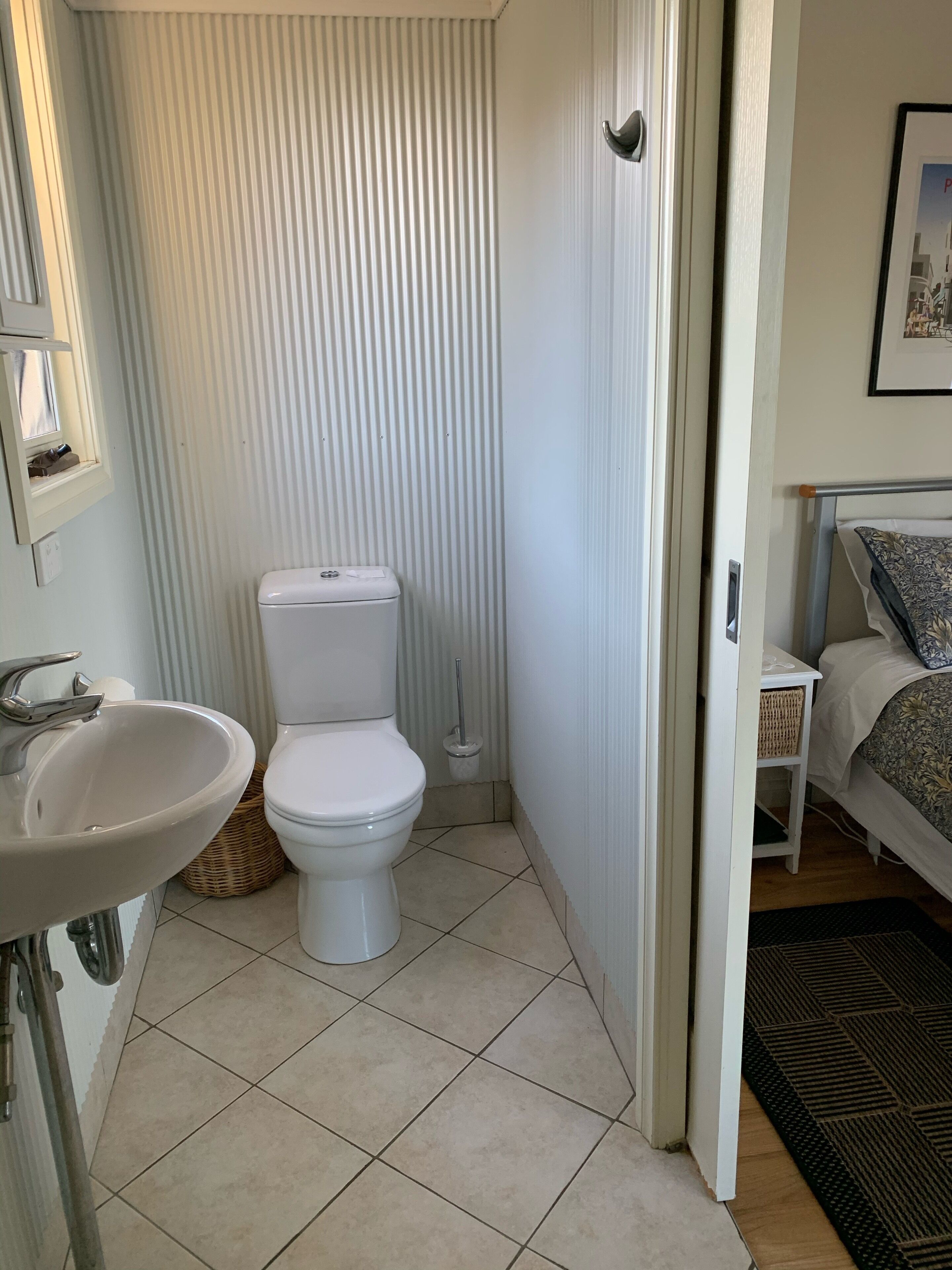 Un baño pequeño y limpio con inodoro, lavamanos y una mesita de noche con una cesta.