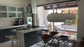 A modern kitchen with a glass island, bar stools, and a dining area with a glass table and chairs. - Villa Ines, sul mare con piscina (CAPOTERRA)