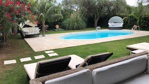 A backyard with a swimming pool, a wicker sofa, and a lounge chair. - Villa Ines, sul mare con piscina (CAPOTERRA)