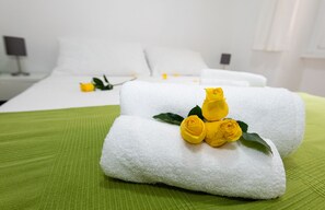 Un lit bien fait, avec des draps blancs et une couvre-lit verte, agrémenté d’une composition décorative de roses jaunes posées sur les oreillers.