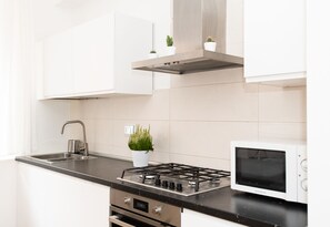 A modern kitchen with white cabinets, a stainless steel stove, a microwave, and a small potted plant.