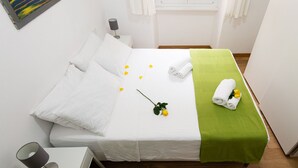 Una cama bien hecha con sábanas blancas, una manta verde y un ramo de flores amarillas.