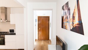Una cocina moderna con armarios blancos, una estufa y un microondas. Una puerta de madera da a un pasillo con piso de madera.