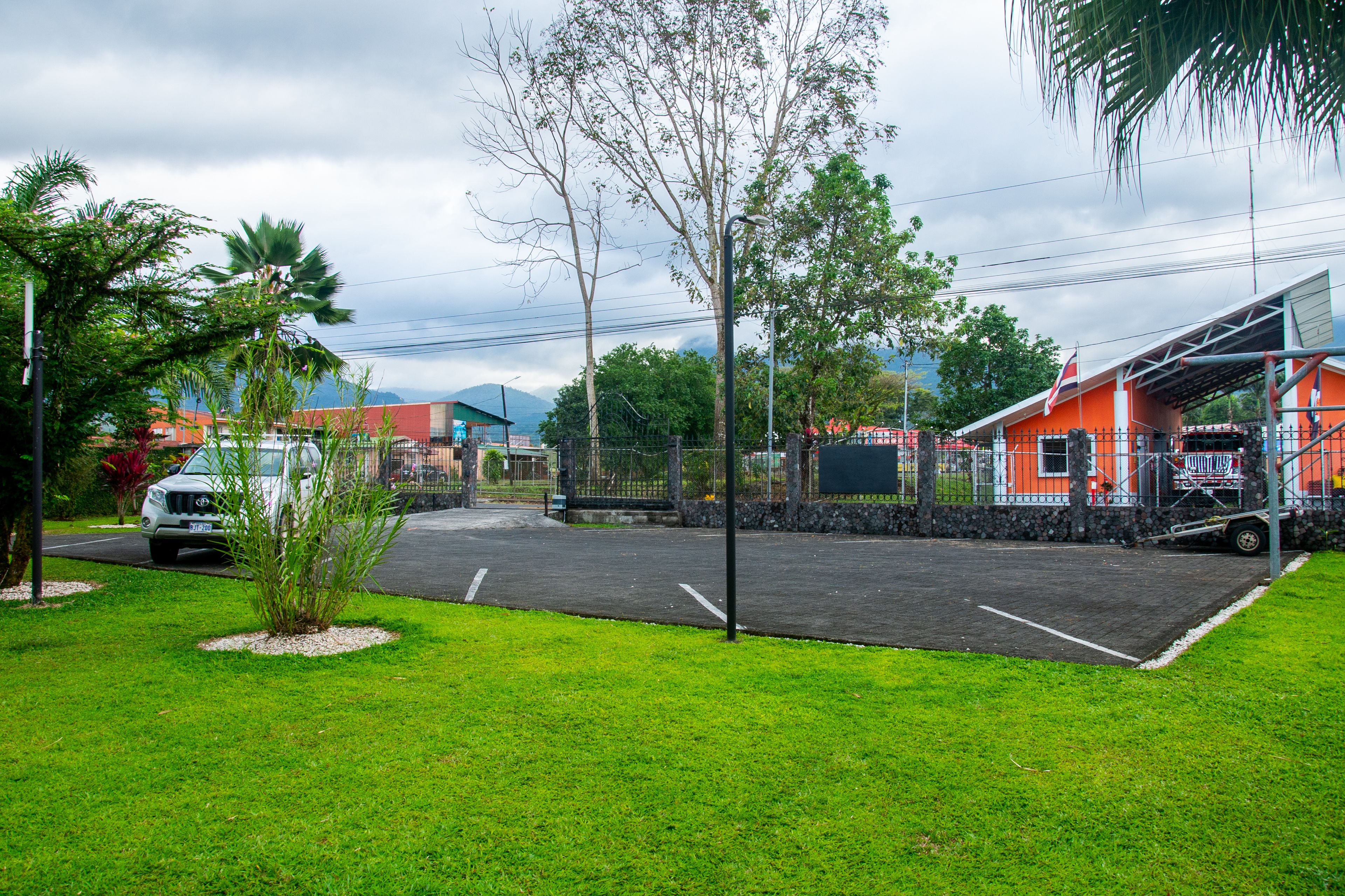 A parking lot with a white truck, a small tree, and a building with a red roof.