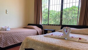 Two beds with beige quilts, a small table, and a window with curtains. - Condos Vista Al Volcán (La Fortuna)