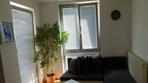 Uma sala de estar com um sofá preto, uma mesa de centro branca e uma planta em vaso.