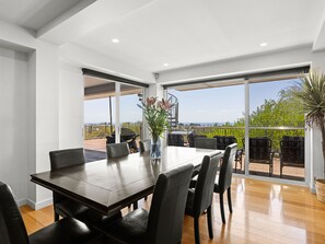 A dining area with a table and chairs, large windows, and a view of greenery and a distant landscape. - Top Class Rye Getaway with Pool (RYE)