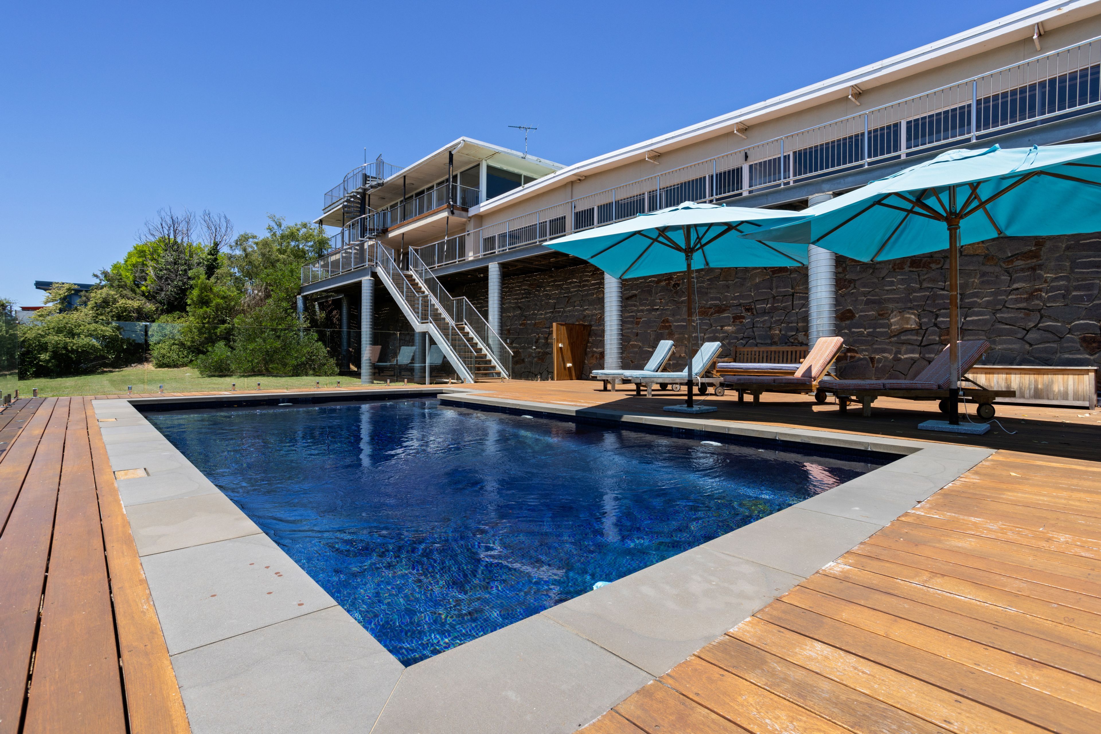 A swimming pool with a wooden deck, lounge chairs, and umbrellas.