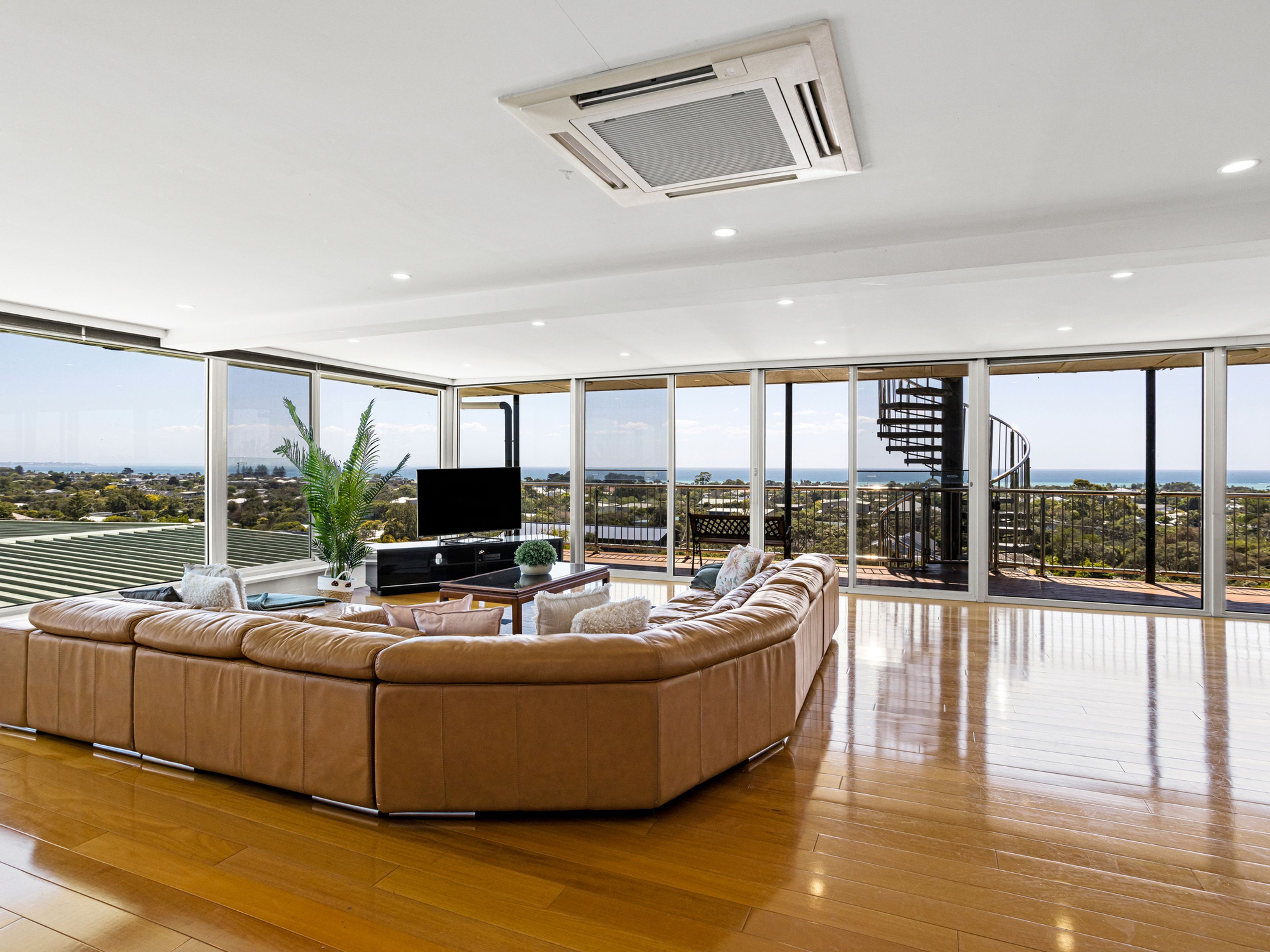 A modern living room with a large sectional sofa, a flat-screen TV, and a view of a cityscape through large windows.