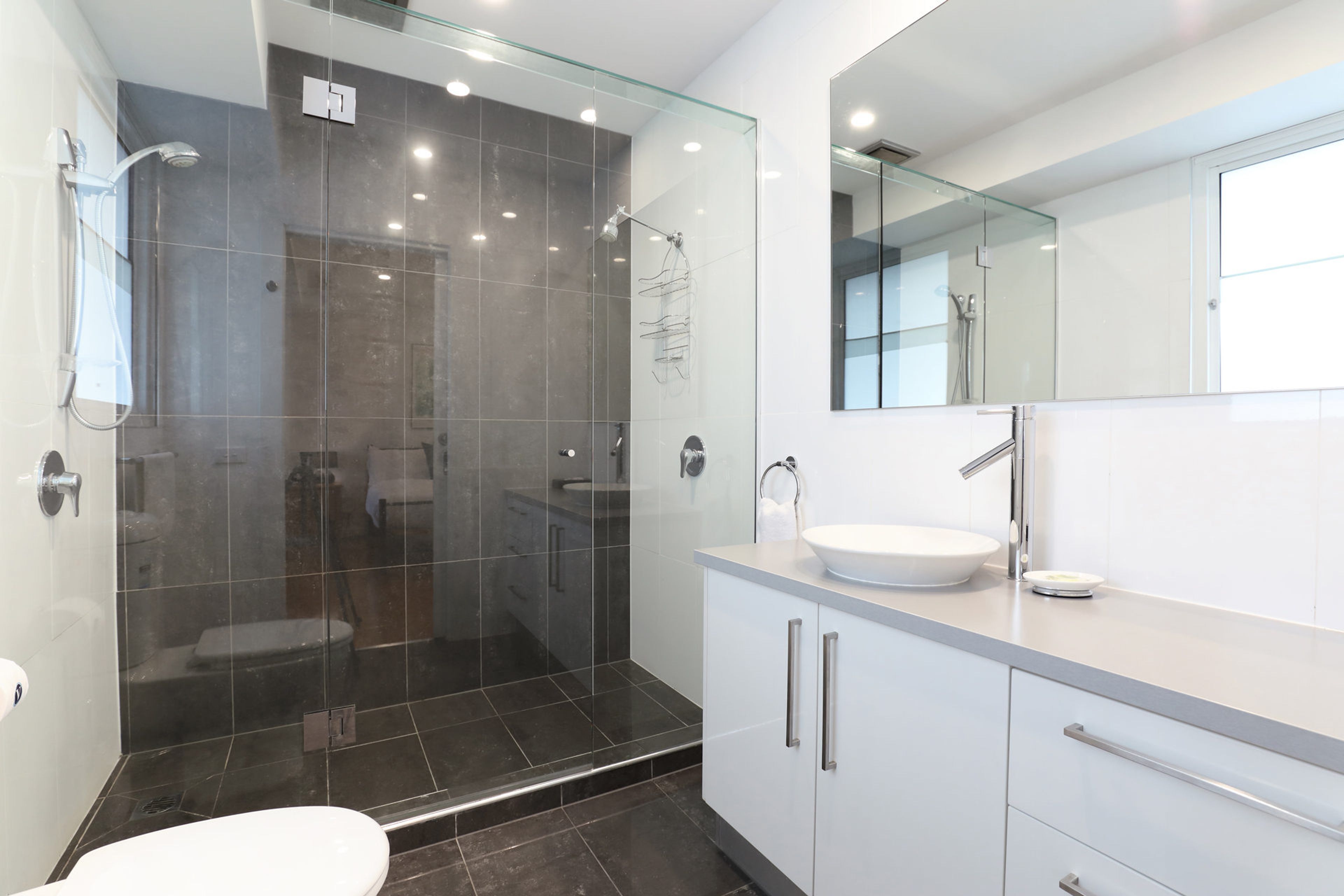 Une salle de bain moderne avec une douche à parois de verre, un lavabo blanc et un grand miroir.