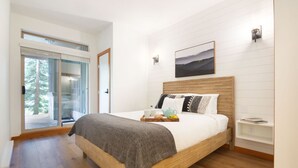 Un dormitorio moderno con una cama de madera, un ventanal de vidrio a un balcón y un cuadro en la pared.