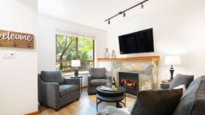 Una sala de estar moderna con chimenea de piedra, sofás grises y un televisor de pantalla plana montado sobre la chimenea.