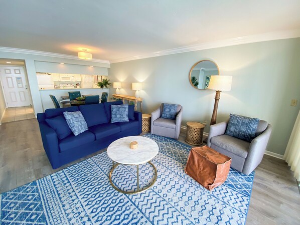 Una sala de estar con un sofá azul, dos sillones, una mesa de centro y una alfombra estampada.