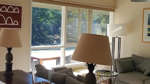 A living room with a sofa, two lamps, a coffee table, and a view of greenery outside. - Riverside House on the beautiful Howqua River (Howqua)