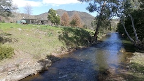 A river flowing through a grassy area with a house in the background. - Riverside House on the beautiful Howqua River (Howqua)