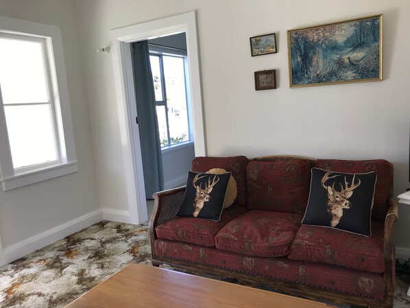 A living room with a red sofa, two decorative pillows with deer images, a wooden coffee table, and a painting on the wall.
