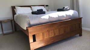 Una cama bien hecha con estructura de madera, ropa de cama blanca y dos toallas dobladas.