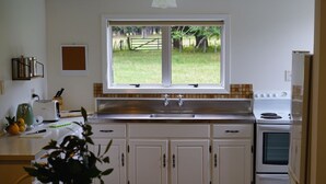 Una cocina con armarios blancos, una ventana, un fregadero, una estufa y una zona de comedor con mesa y sillas.