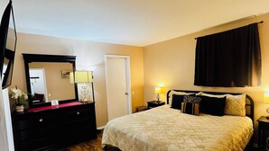 Una camera da letto con un letto grande, una cassettiera, uno specchio, una porta e una bocchetta di ventilazione al soffitto.
