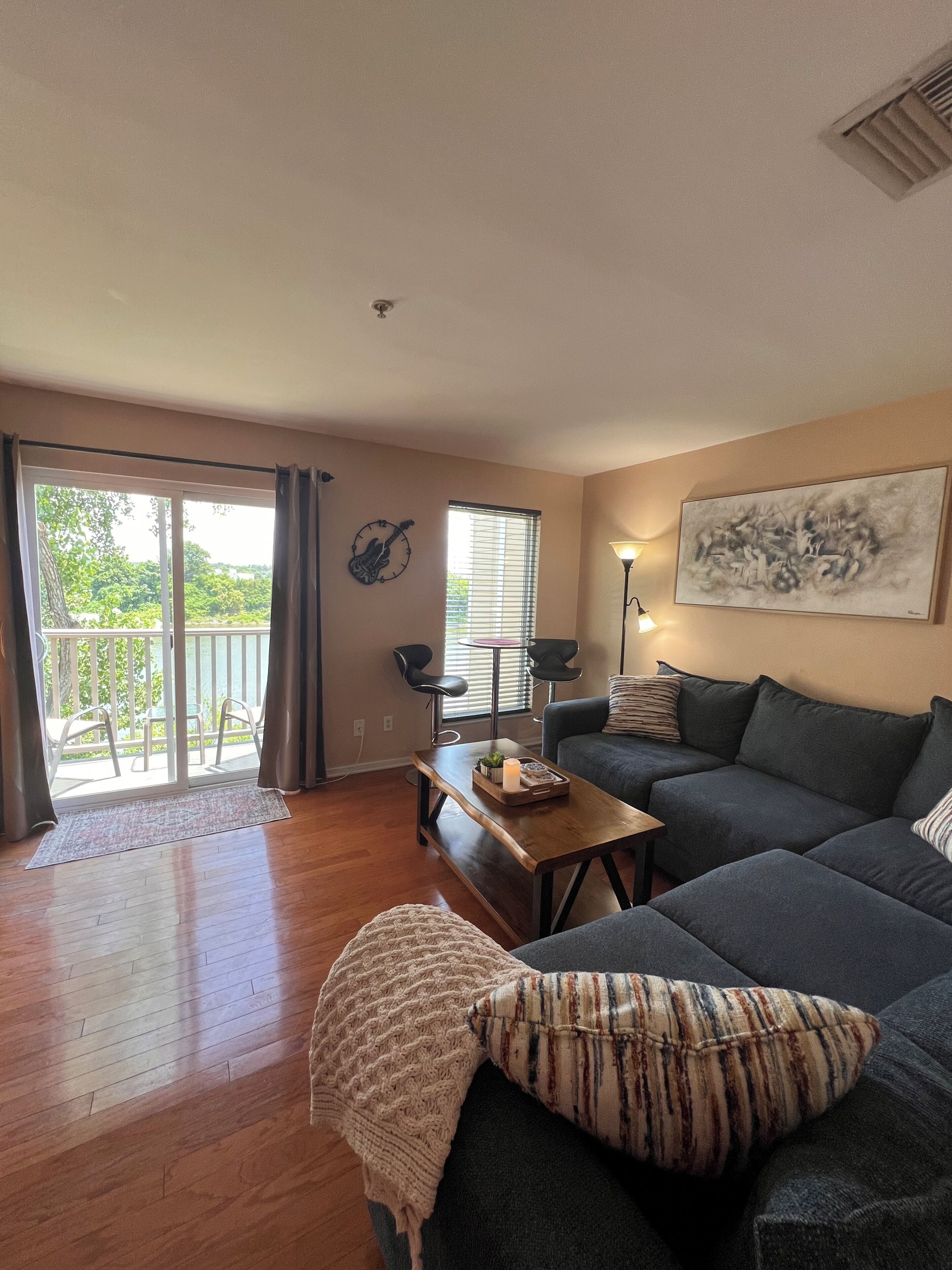 A living room with a sofa, a coffee table, a lamp, a painting, and a view through the sliding glass door.