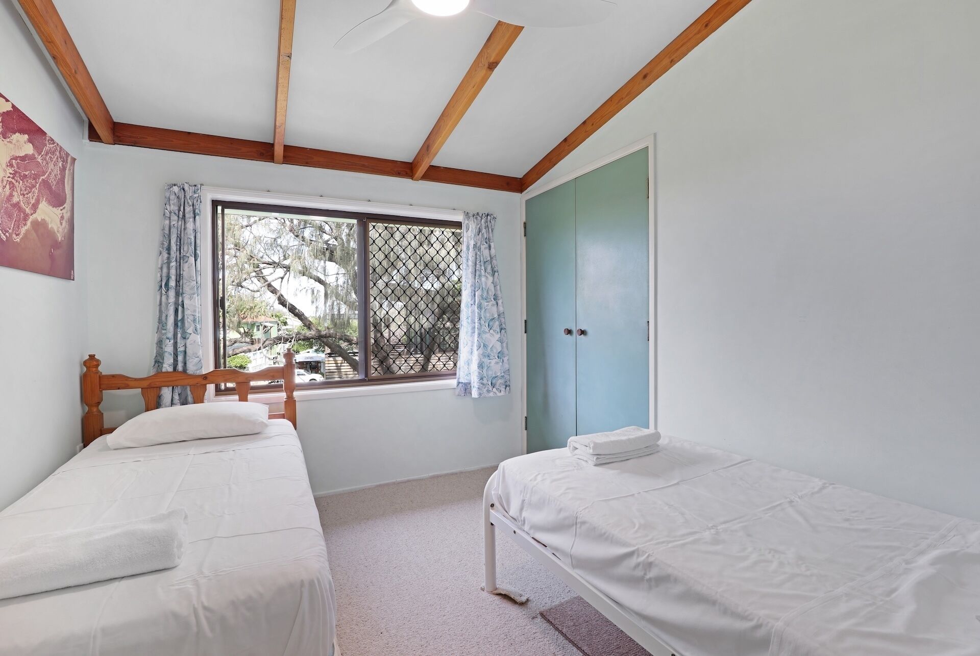 A room with two single beds, a window with curtains, a door, and a ceiling fan.