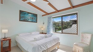 A bedroom with a bed, a window with a view, a chair, and a painting on the wall.