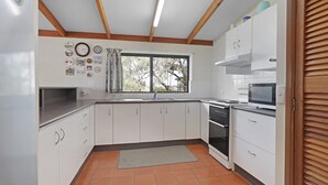 A kitchen with white cabinets, a stove, an oven, a microwave, and a window with curtains.