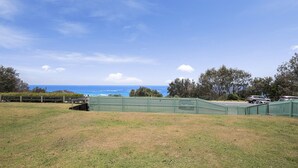 A grassy field with a green fence, trees, and a view of the ocean.