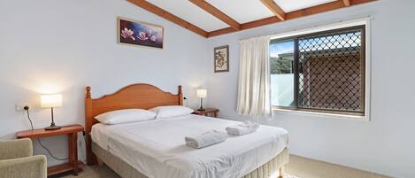 Un dormitorio con una cama de madera, dos mesitas de noche con lámparas, una ventana con cortinas y un cuadro en la pared.