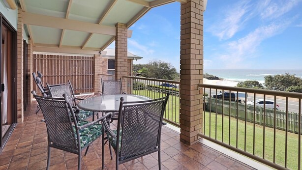 A covered patio with a round table and chairs, a brick pillar, and a view of the ocean.