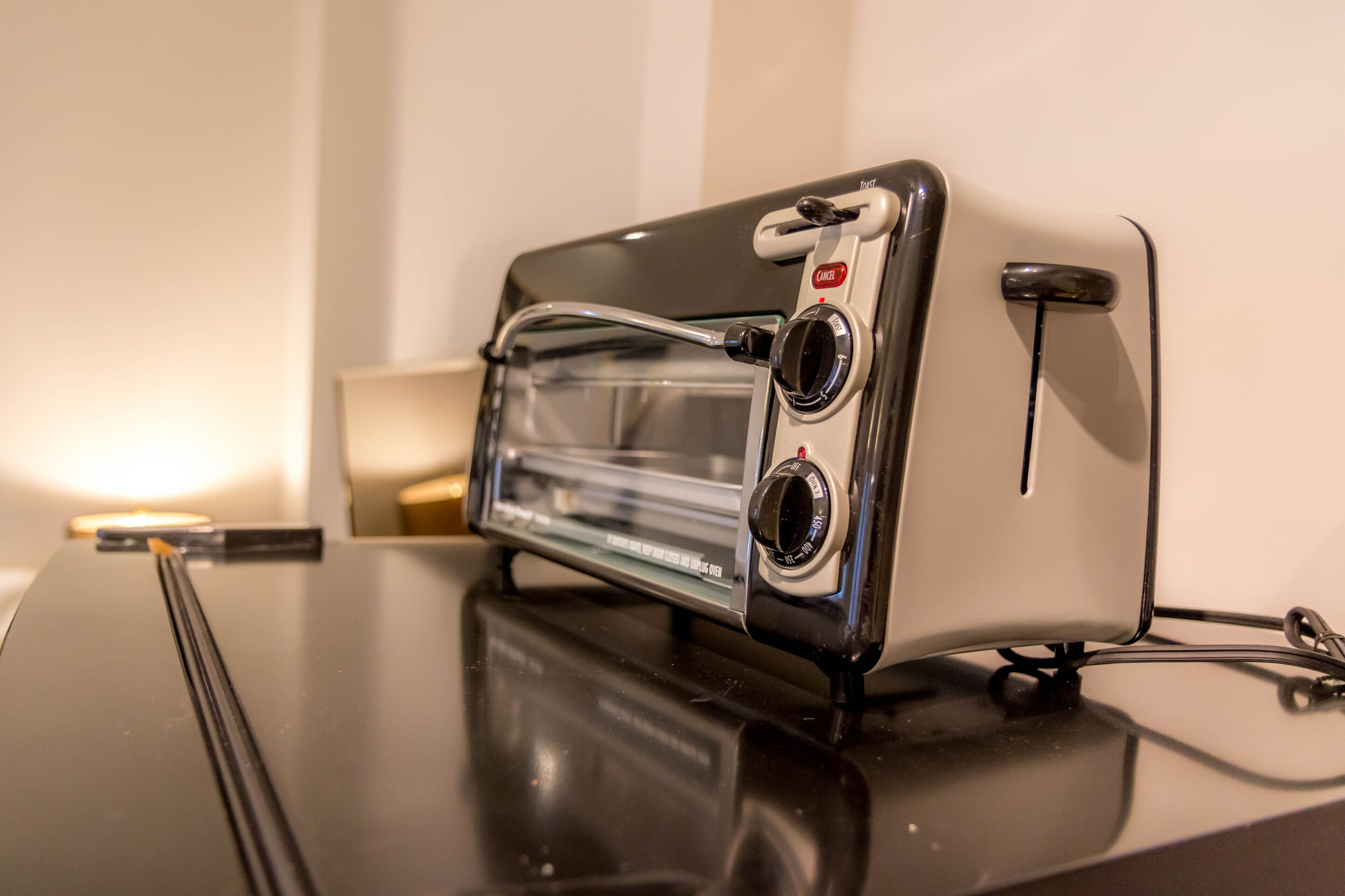 A black toaster oven with two control knobs and a power cord on a reflective black countertop.