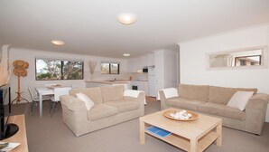 A modern living room with two beige sofas, a wooden coffee table, and a dining area with a white table and chairs. - Promenade 11, 8 Intrepid Close - air conditioned unit with beautiful water views (Nelson Bay)