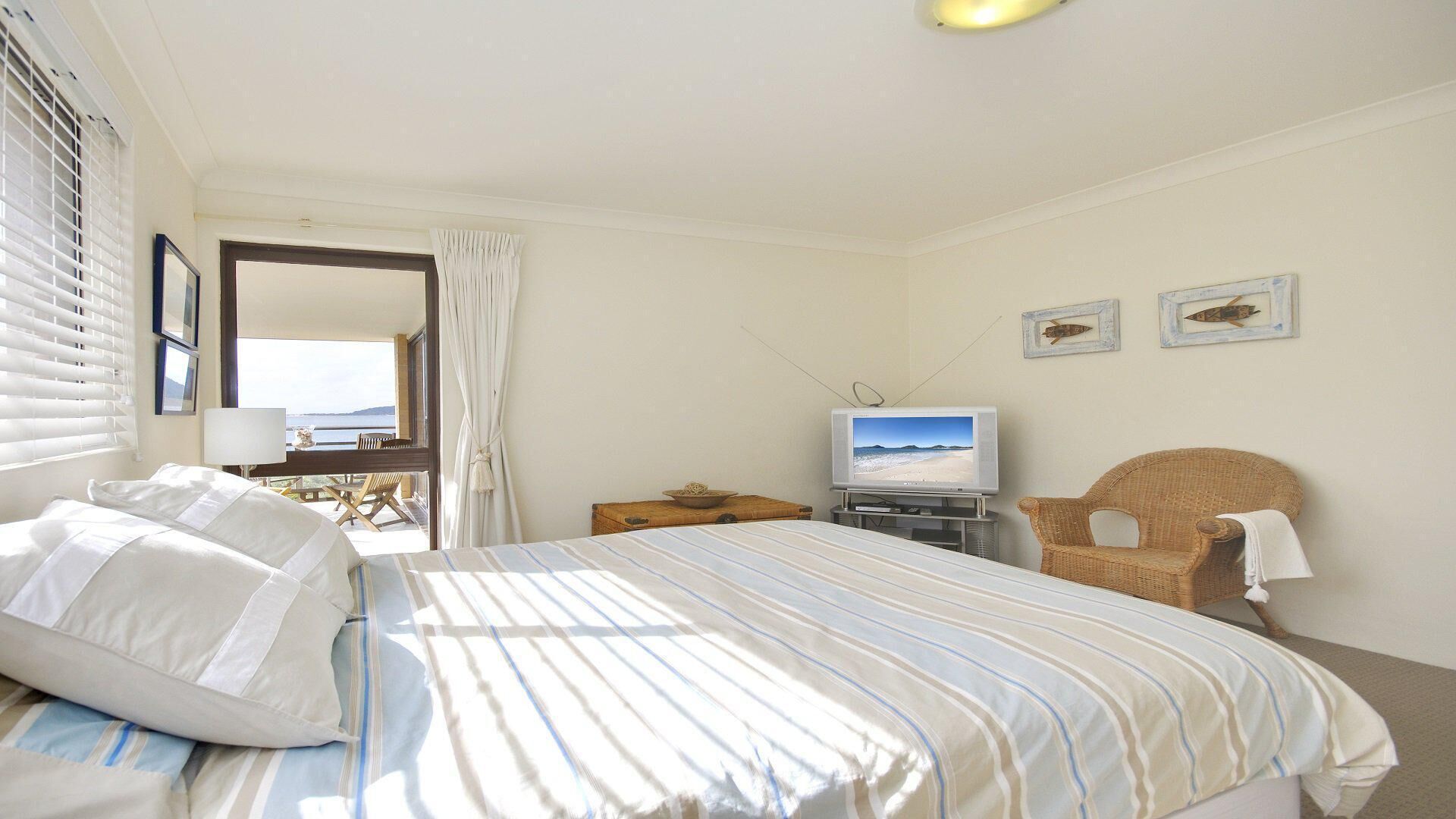 A hotel room with a bed, a television, a wicker chair, and a view of the sea through the window.