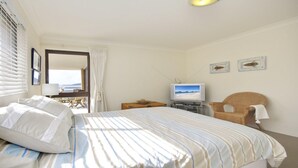 A hotel room with a bed, a television, a wicker chair, and a view of the sea through the window. - Promenade 11, 8 Intrepid Close - air conditioned unit with beautiful water views (Nelson Bay)