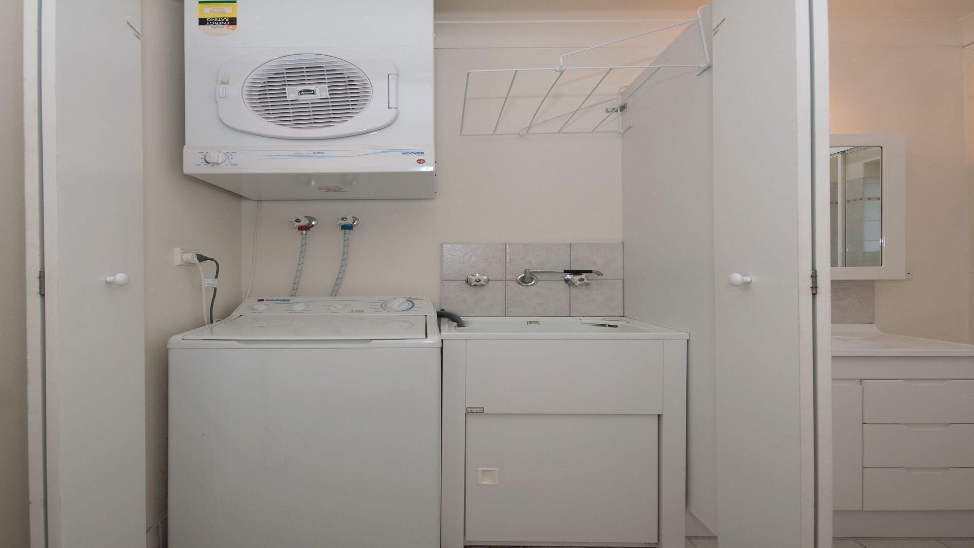 A compact laundry area with a front-loading washer and dryer, a wall-mounted drying rack, and a small sink with a mirror above it.