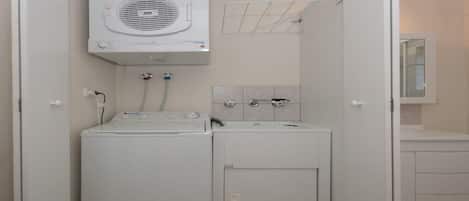 A compact laundry area with a front-loading washer and dryer, a wall-mounted drying rack, and a small sink with a mirror above it.