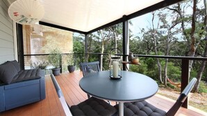 Un área de estar al aire libre techada con una mesa redonda, bancos acolchados y un paraguas decorativo.