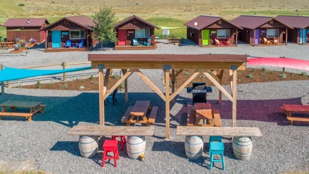 Un camping con cabañas de madera, mesas de picnic y barriles.
