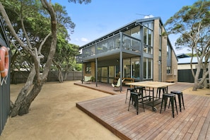 Une maison à deux étages dotée d’une terrasse, d’un espace salon extérieur et d’un jardin clôturé.