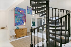 Un intérieur moderne avec un escalier en colimaçon, des œuvres d’art abstrait accrochées aux murs et un meuble en bois.