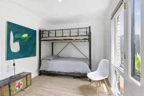 A bunk bed room with a large window, a white chair, and a painting on the wall.