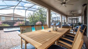 Un patio techado con una mesa y sillas de madera, una piscina y una vista de una casa al fondo.