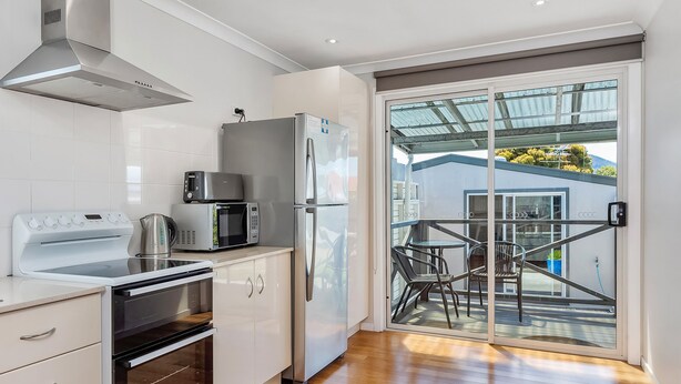 Une cuisine moderne dotée d’appareils électroménagers en acier inoxydable, d’un four encastré et d’une porte-fenêtre coulissante donnant sur un balcon avec coin salon extérieur.