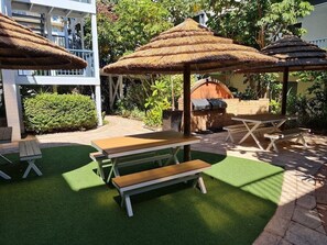 An outdoor patio with thatched umbrellas, picnic tables, and a barbecue grill. - Scarborough Beach Escape NEW (Scarborough)